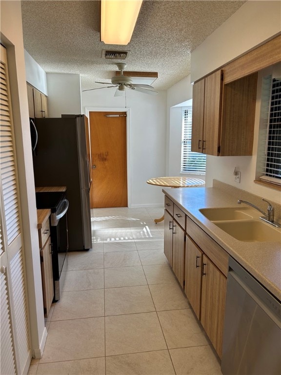 kitchen featuring sink, ceiling fan, light tile patterned floors, a textured ceiling, and appliances with stainless steel finishes