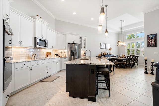 kitchen featuring stainless steel appliances, white cabinetry, hanging light fixtures, sink, and an island with sink