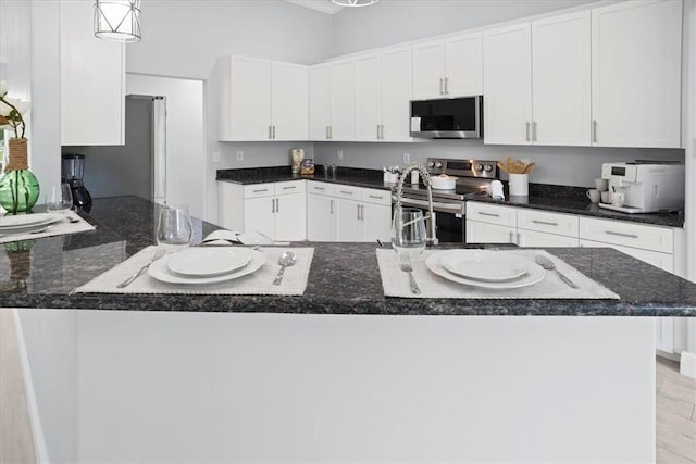 614 Stevenson Ave, Sebastian, FL 32958 - kitchen with stainless steel appliances, white cabinets, dark stone counters, decorative light fixtures, and a peninsula