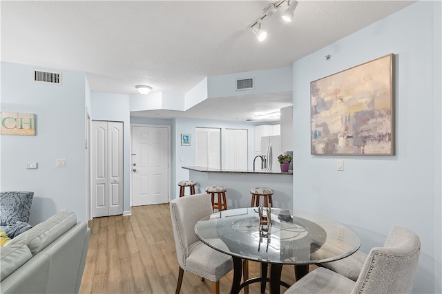 dining area with light wood-type flooring, a textured ceiling, and track lighting