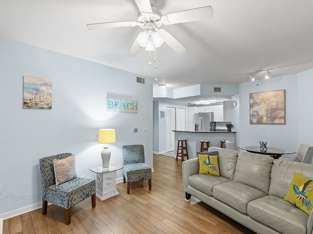 living room featuring ceiling fan, light wood-type flooring, and a textured ceiling