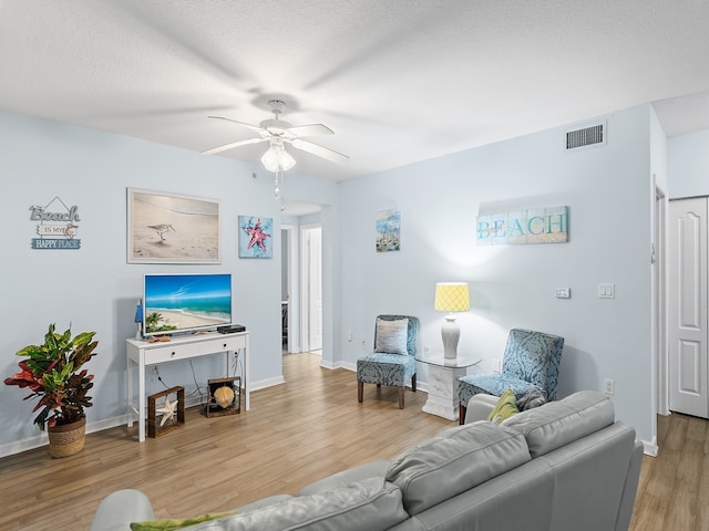 living room featuring ceiling fan, a textured ceiling, and light wood-type flooring