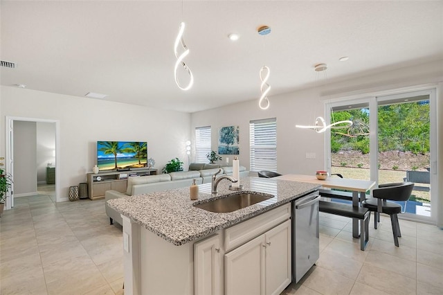 kitchen featuring pendant lighting, a center island with sink, a sink, stainless steel dishwasher, and light stone countertops