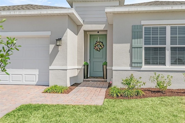 view of exterior entry with stucco siding, driveway, and an attached garage