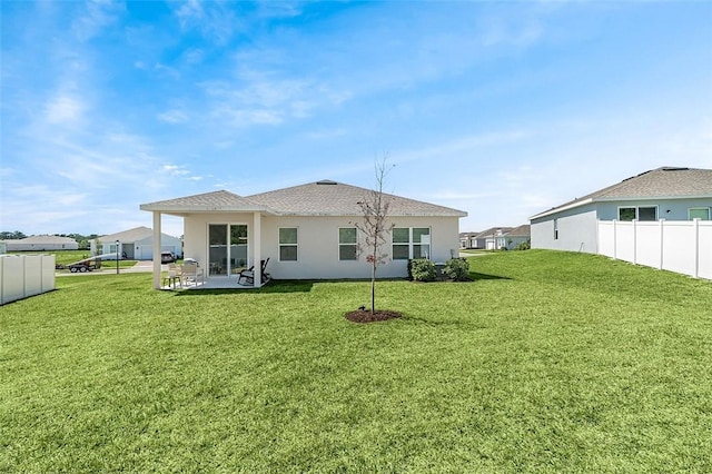 rear view of property with stucco siding, a patio, a yard, and fence