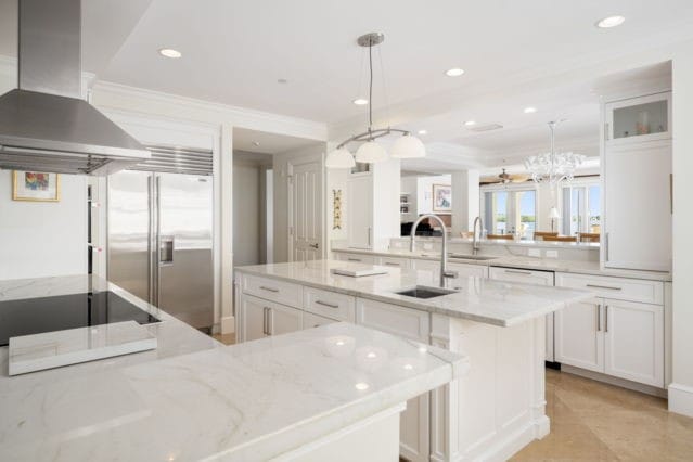 kitchen with a kitchen island with sink, stainless steel built in refrigerator, a sink, white cabinets, and wall chimney range hood