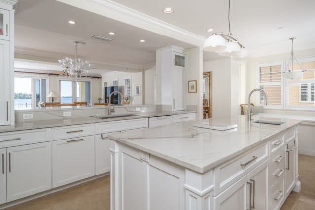 kitchen with a sink, a kitchen island with sink, ornamental molding, and white cabinets