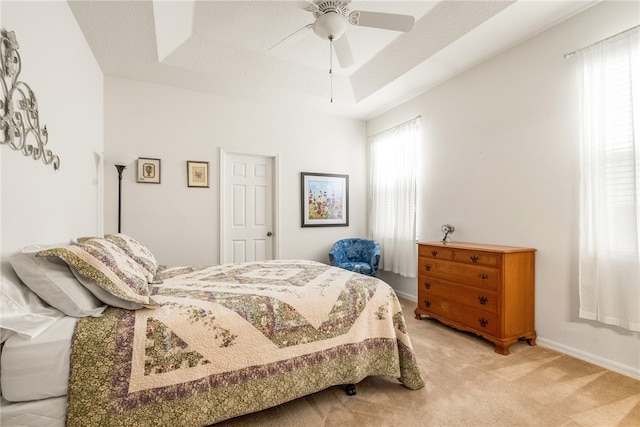 bedroom featuring ceiling fan, a textured ceiling, light carpet, and a tray ceiling