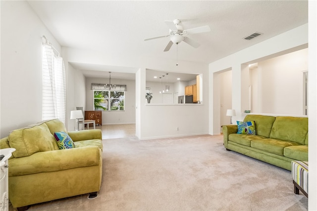 carpeted living room featuring ceiling fan with notable chandelier