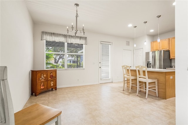 kitchen with stainless steel fridge, light brown cabinetry, hanging light fixtures, an inviting chandelier, and a kitchen breakfast bar