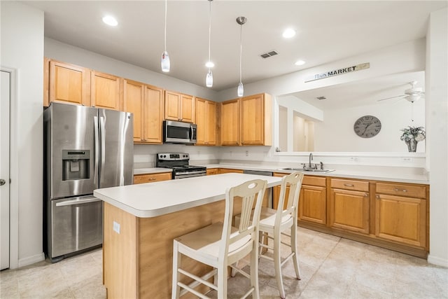 kitchen with a center island, hanging light fixtures, ceiling fan, a breakfast bar, and appliances with stainless steel finishes