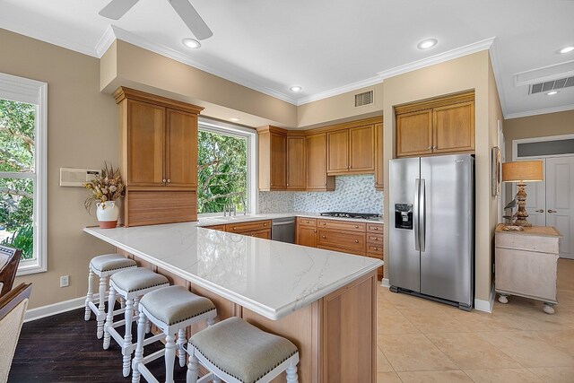 kitchen featuring plenty of natural light, kitchen peninsula, crown molding, and stainless steel appliances