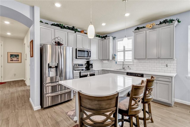 kitchen featuring gray cabinetry, decorative light fixtures, stainless steel appliances, and light wood-type flooring