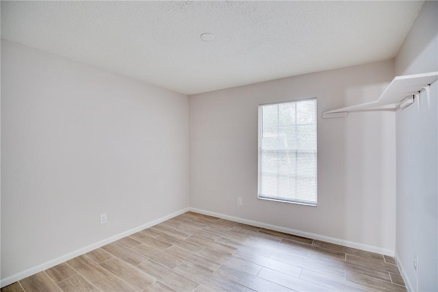 unfurnished room with wood tiled floor, a textured ceiling, and baseboards