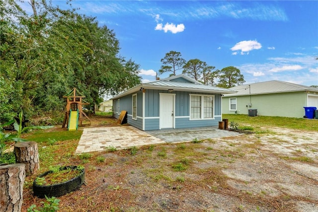 rear view of house with a playground, a patio, board and batten siding, metal roof, and cooling unit