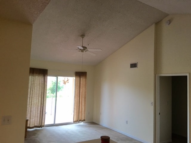 unfurnished room featuring ceiling fan, a textured ceiling, vaulted ceiling, and light colored carpet