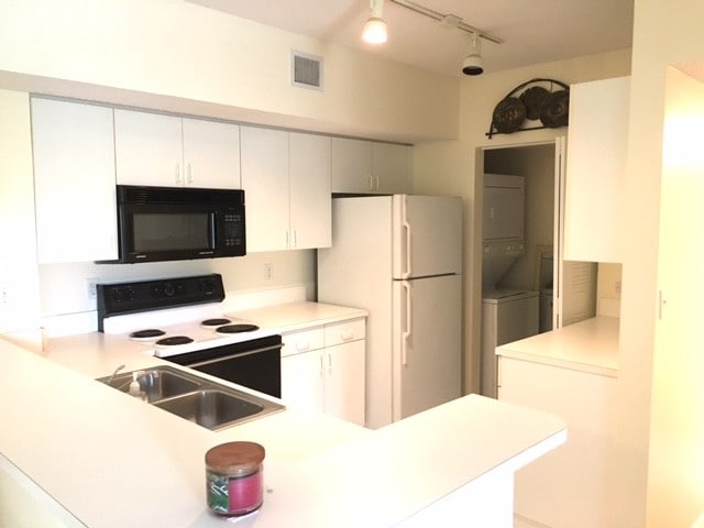 kitchen featuring white appliances, sink, stacked washer and dryer, and white cabinets