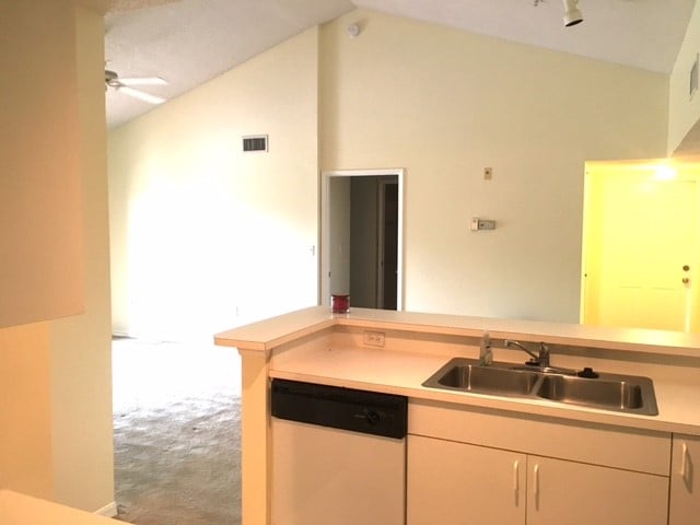 kitchen with sink, vaulted ceiling, white cabinets, dishwasher, and ceiling fan