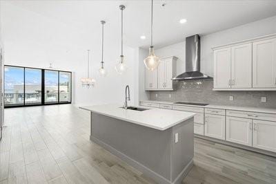 225 Strand Dr Unit 204, Melbourne Beach, FL 32951 - kitchen with wall chimney exhaust hood, light wood-type flooring, light countertops, decorative backsplash, and a center island with sink