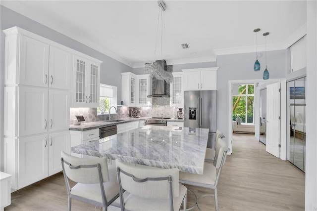 kitchen featuring wall chimney range hood, white cabinetry, a sink, a kitchen island, and backsplash