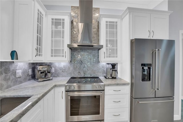 kitchen featuring wall chimney range hood, light stone counters, decorative backsplash, white cabinets, and stainless steel appliances