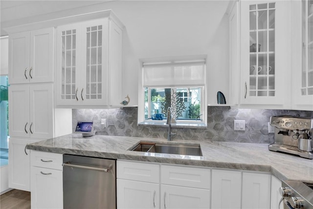 kitchen featuring stove, light stone countertops, white cabinetry, and a sink