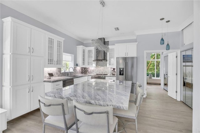 kitchen with wall chimney range hood, white cabinets, backsplash, a sink, and a center island