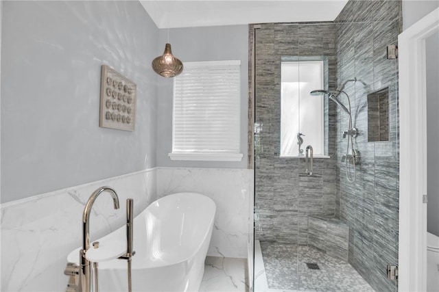 bathroom featuring tile walls, a stall shower, marble finish floor, a freestanding bath, and a wainscoted wall
