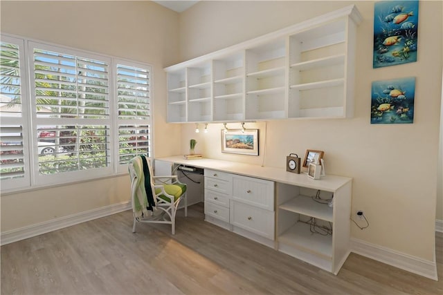 office with light wood-type flooring, baseboards, and built in desk
