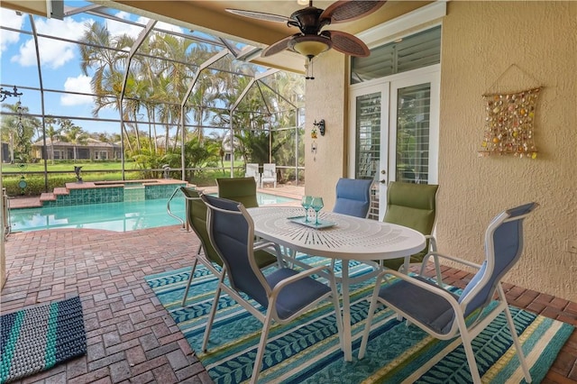 view of patio with glass enclosure, outdoor dining area, a pool with connected hot tub, and a ceiling fan
