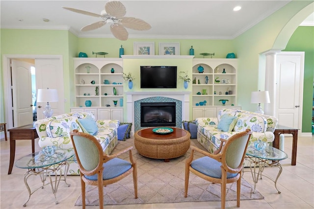 living room featuring arched walkways, ornamental molding, a glass covered fireplace, a ceiling fan, and tile patterned floors