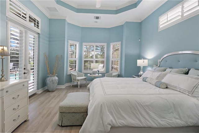 bedroom with light wood-type flooring, visible vents, ornamental molding, and a raised ceiling