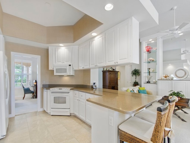 kitchen featuring white cabinetry, ceiling fan, a kitchen breakfast bar, kitchen peninsula, and white appliances