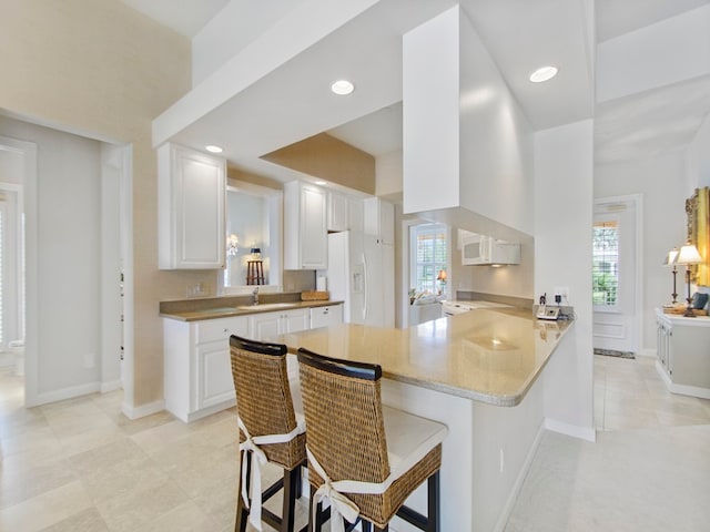 kitchen featuring a breakfast bar area, white cabinets, white appliances, and kitchen peninsula