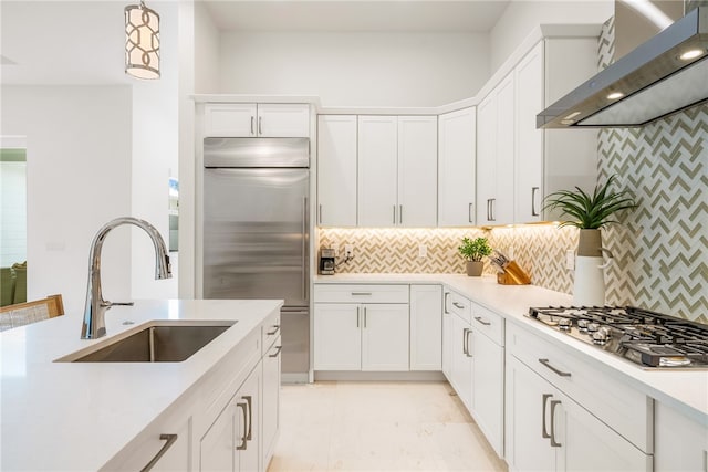 kitchen with stainless steel appliances, white cabinets, wall chimney exhaust hood, sink, and decorative light fixtures