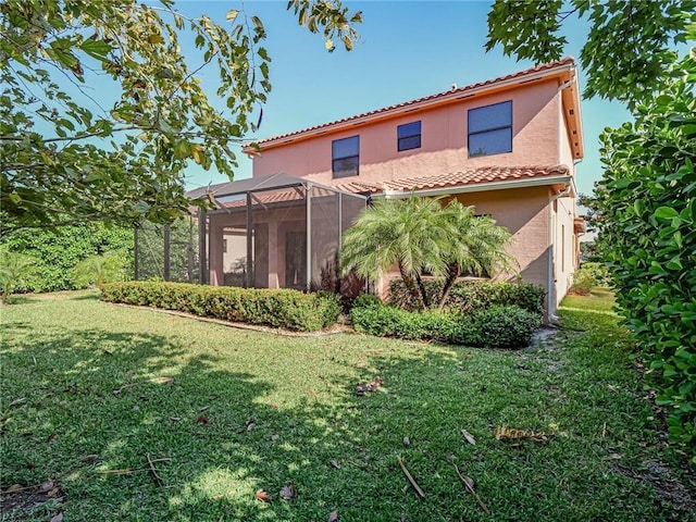 rear view of property with glass enclosure and a lawn