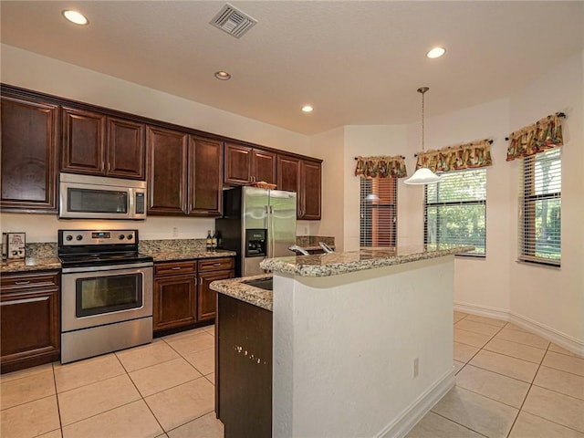 kitchen with hanging light fixtures, light tile patterned floors, appliances with stainless steel finishes, and an island with sink