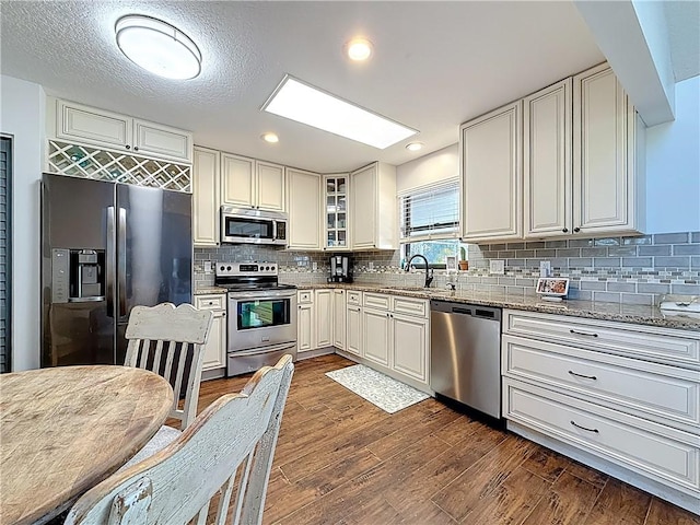 kitchen featuring a sink, light stone counters, tasteful backsplash, dark wood-style floors, and stainless steel appliances