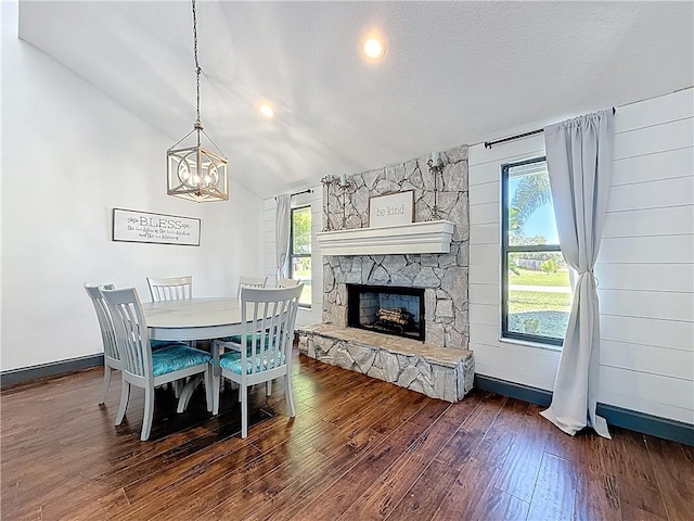 dining area with lofted ceiling, hardwood / wood-style flooring, a stone fireplace, and a wealth of natural light