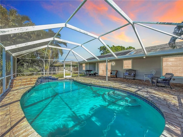 pool at dusk featuring glass enclosure, a patio, and an outdoor pool