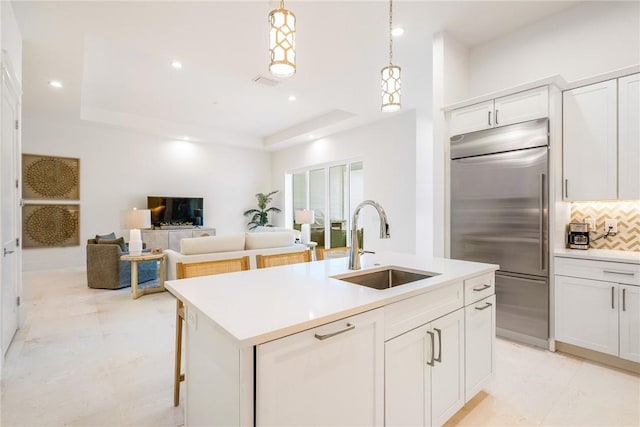 30 Strand Dr, Vero Beach, FL 32963 - kitchen featuring stainless steel built in refrigerator, a tray ceiling, tasteful backsplash, a center island with sink, and light countertops