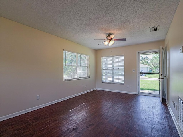 spare room featuring visible vents, dark wood-type flooring, a ceiling fan, a textured ceiling, and baseboards