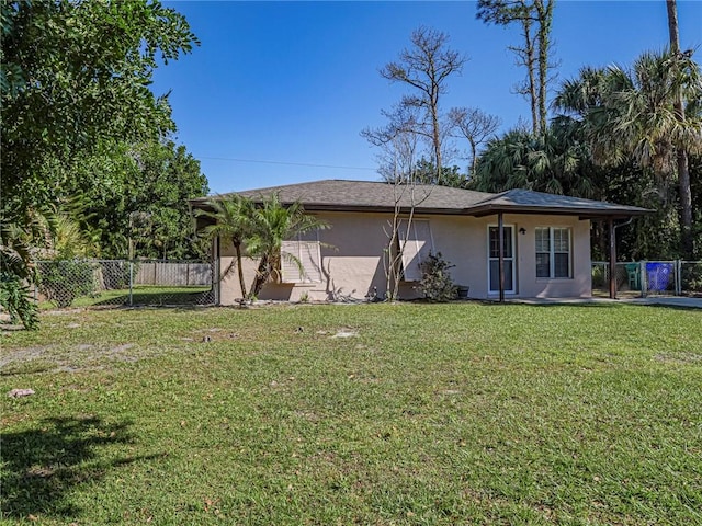 back of house with stucco siding, a yard, and fence