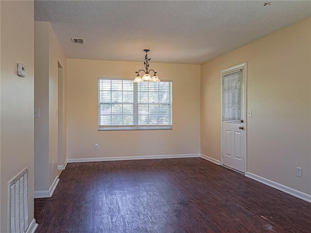 unfurnished room with baseboards, wood finished floors, visible vents, and a chandelier