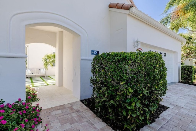 view of exterior entry featuring stucco siding, decorative driveway, and a garage