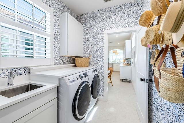 clothes washing area featuring a sink, cabinet space, wallpapered walls, light tile patterned floors, and washing machine and clothes dryer