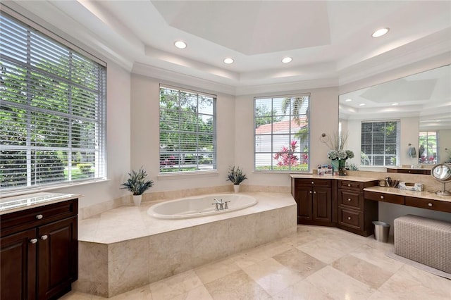 bathroom featuring vanity, a tray ceiling, tiled bath, and a healthy amount of sunlight