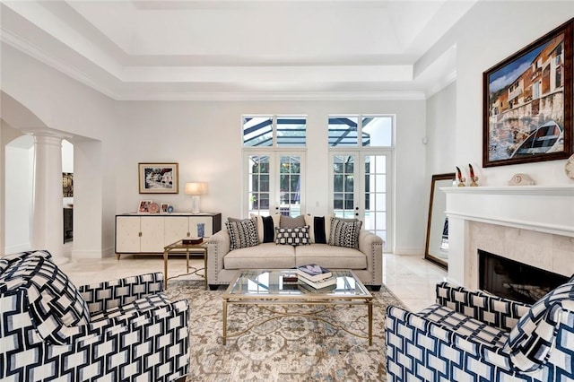 living room featuring a premium fireplace, a high ceiling, a raised ceiling, french doors, and ornate columns