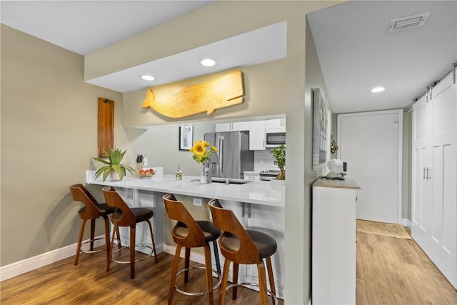 31 Plantation Dr Unit 205, Vero Beach, FL 32966 - kitchen featuring a kitchen bar, light wood-type flooring, a peninsula, freestanding refrigerator, and white cabinets