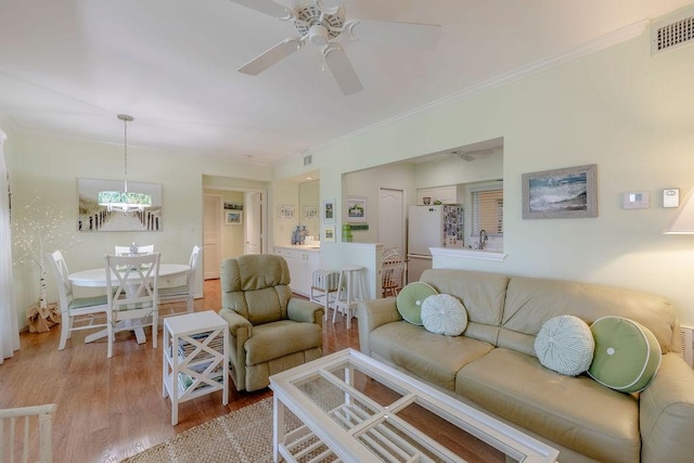 living room with crown molding, a ceiling fan, wood finished floors, and visible vents